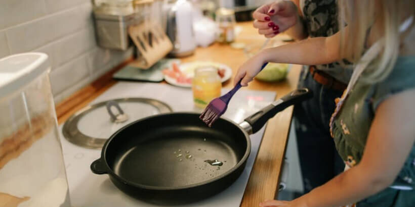 A child holding a wooden spoon over a cast iron pan on the stove.